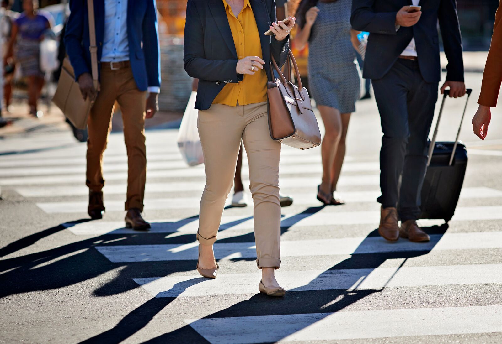 Business people walking on pedestrian crossing, with phones and bags, at sunset