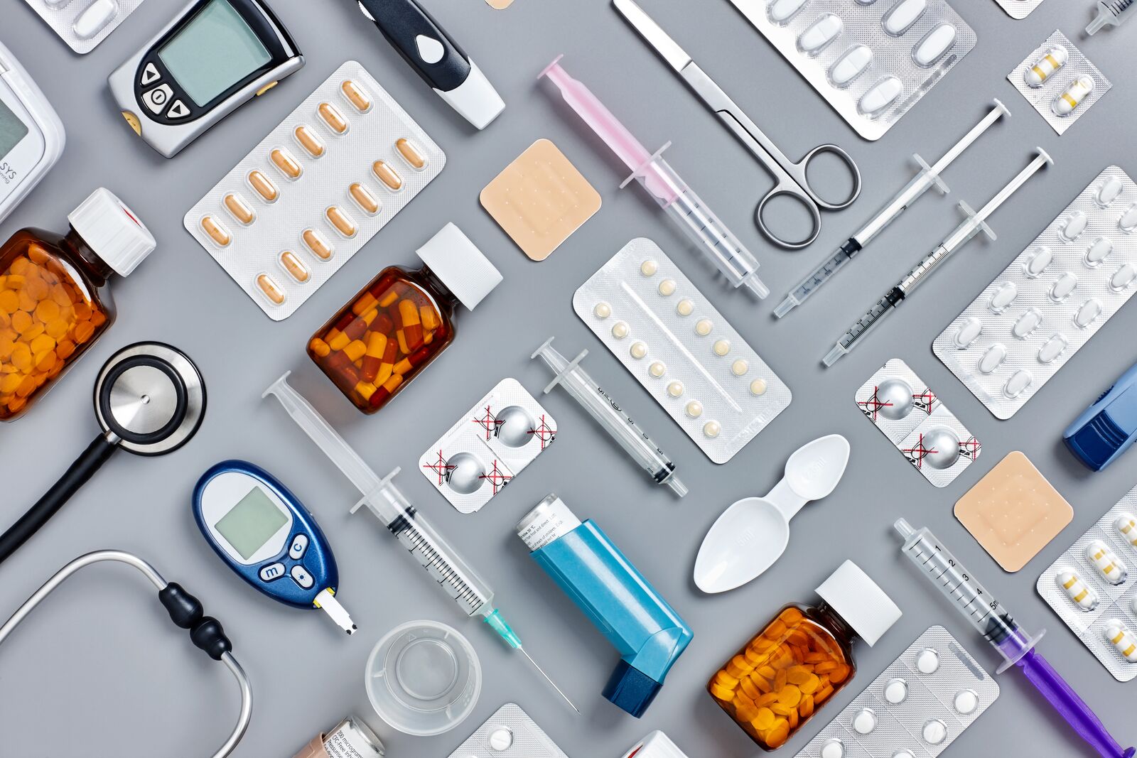 Directly above flat lay flat lay shot of various medical supplies. Full frame shot of medicines placed with syringes and diagnostic tools. All are on gray background. Knolling concept.
