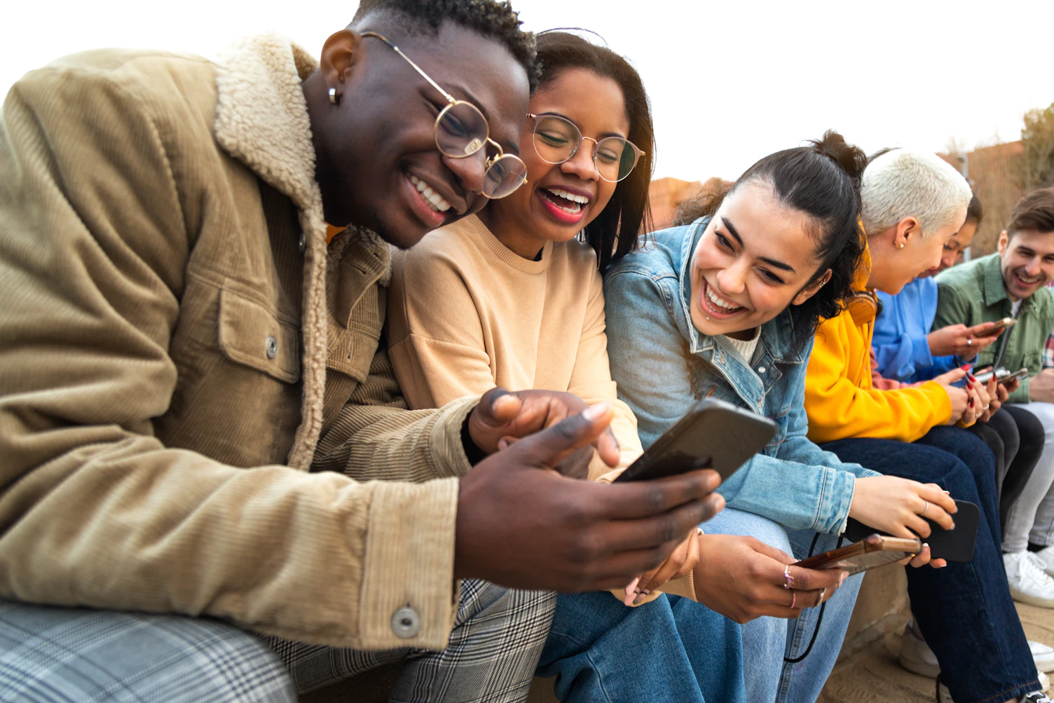 Happy multiracial teen college students having fun using mobile phone together in campus outdoors