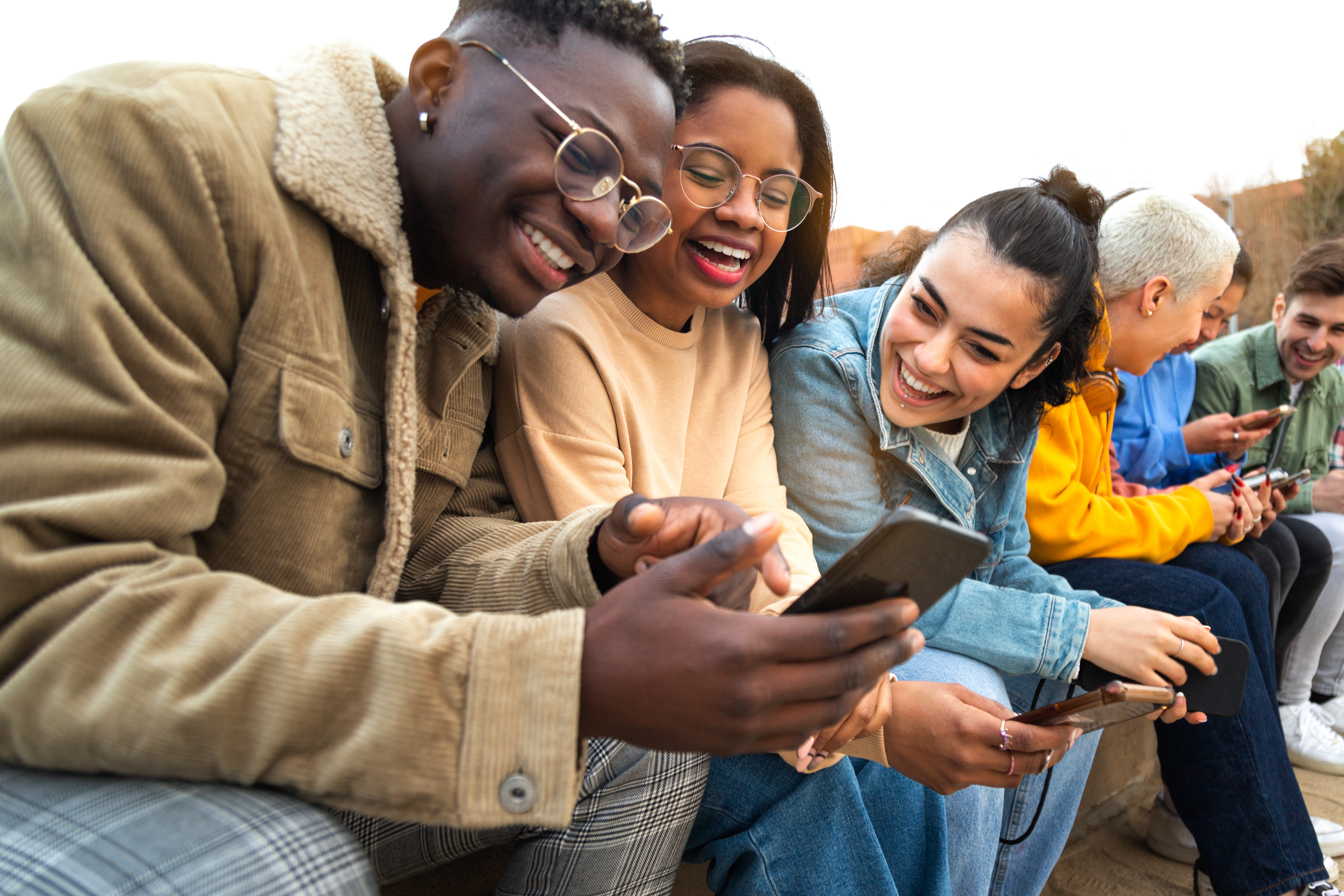 Happy multiracial teen college students having fun using mobile phone together in campus outdoors