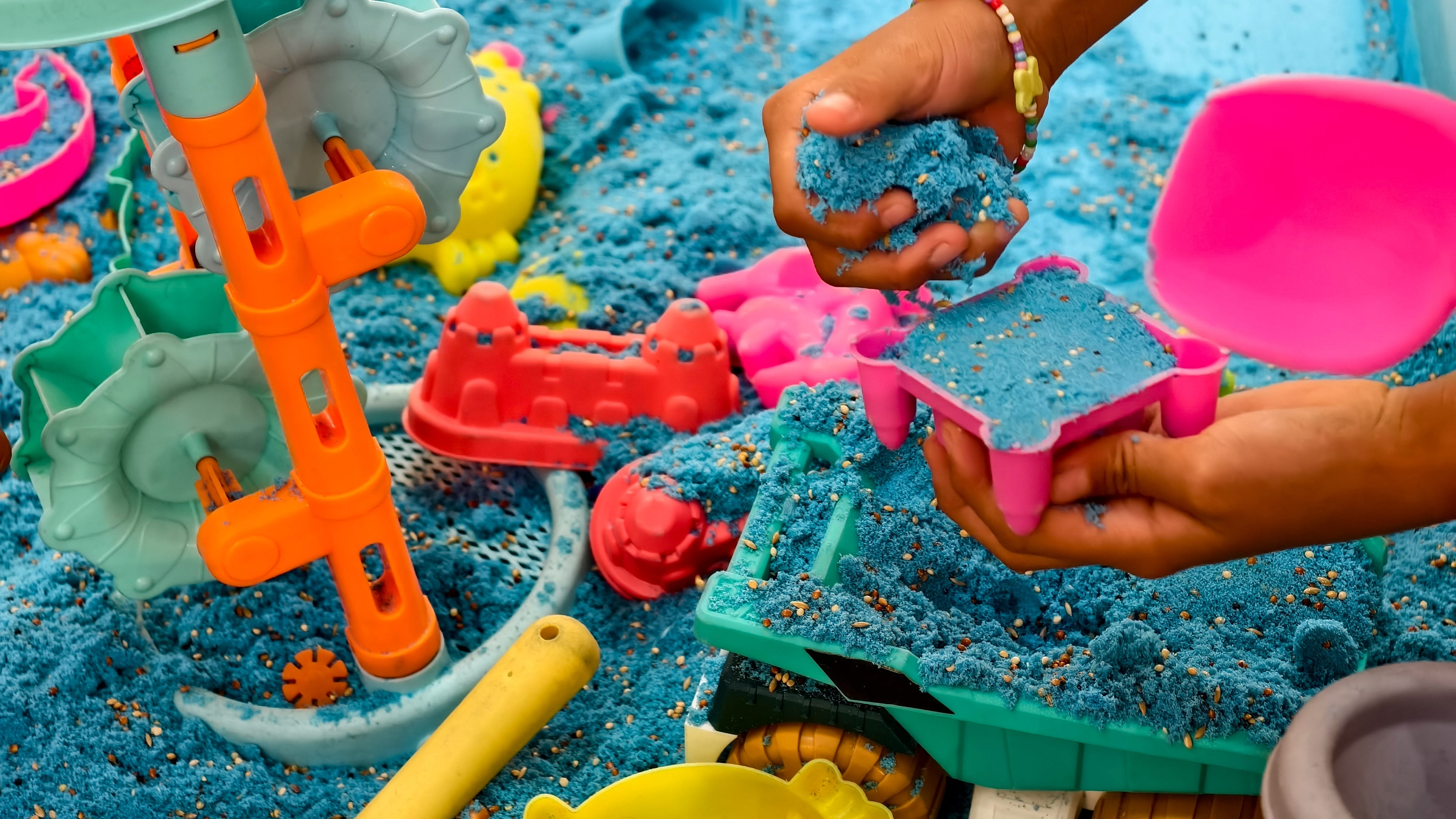 A childs hand plays with blue kinetic sand