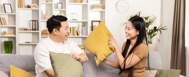 A joyful Asian couple engaging in a playful pillow fight