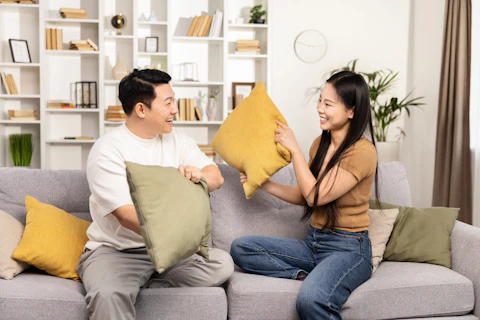 A joyful Asian couple engaging in a playful pillow fight