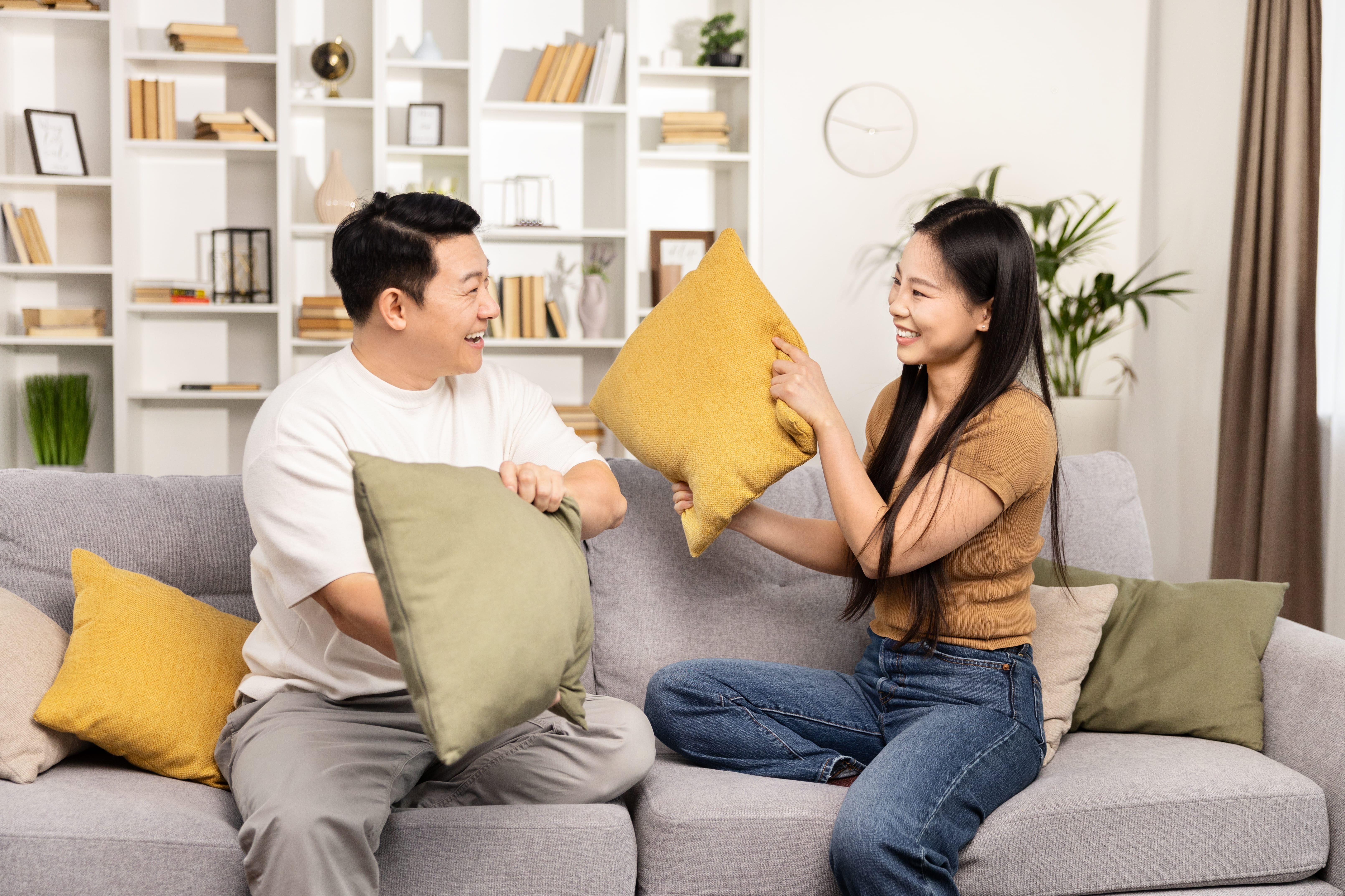 A joyful Asian couple engaging in a playful pillow fight