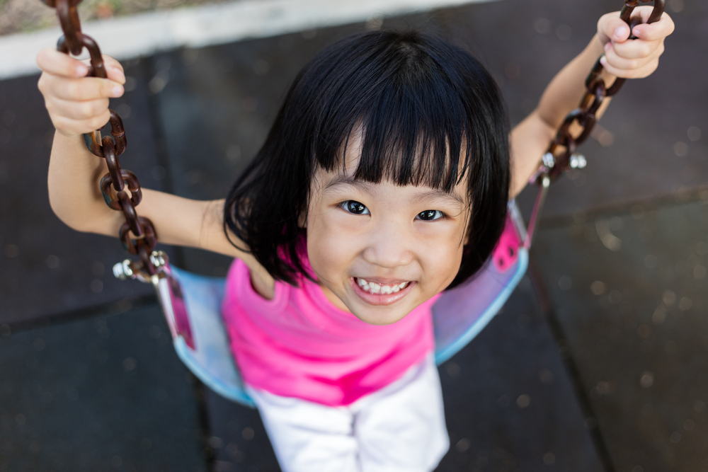 Asian Chinese little girl on swing in playground outdoor