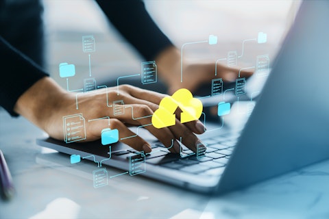 Hands typing on a laptop keyboard with digital icons of folders and a yellow cloud upload symbol, representing cloud data storage and file sharing