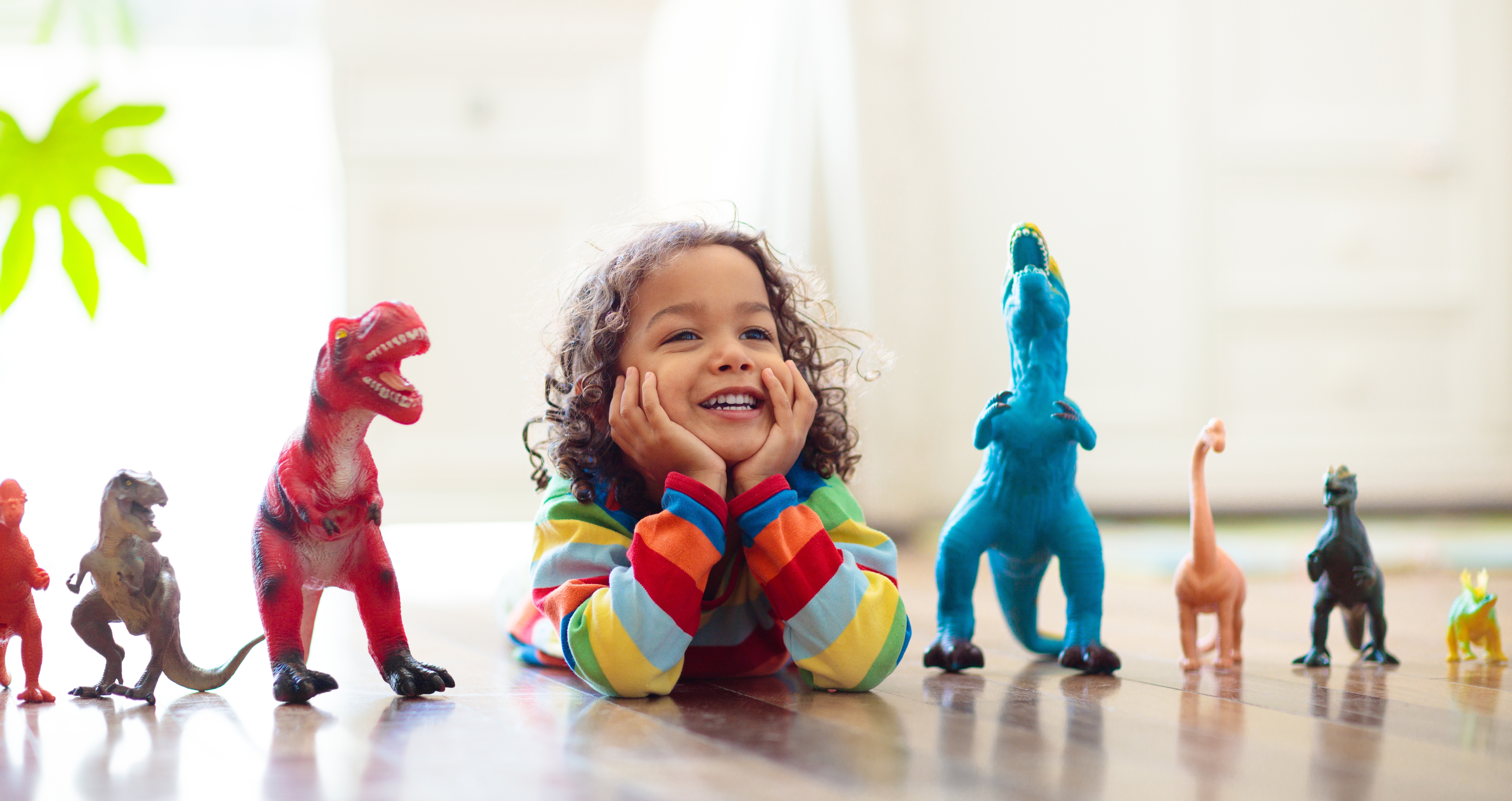 Child wearing a colorful striped sweater surrounded by a row of toy dinosaurs arranged in front