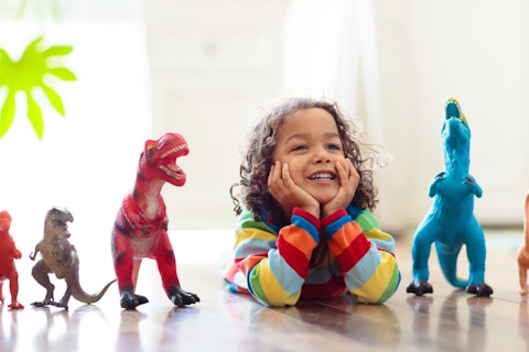 Child wearing a colorful striped sweater surrounded by a row of toy dinosaurs arranged in front