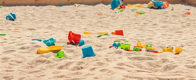 Children’s sandpit with colourful plastic toys and moulds scattered across the sand, including buckets, trucks, and small play tools.