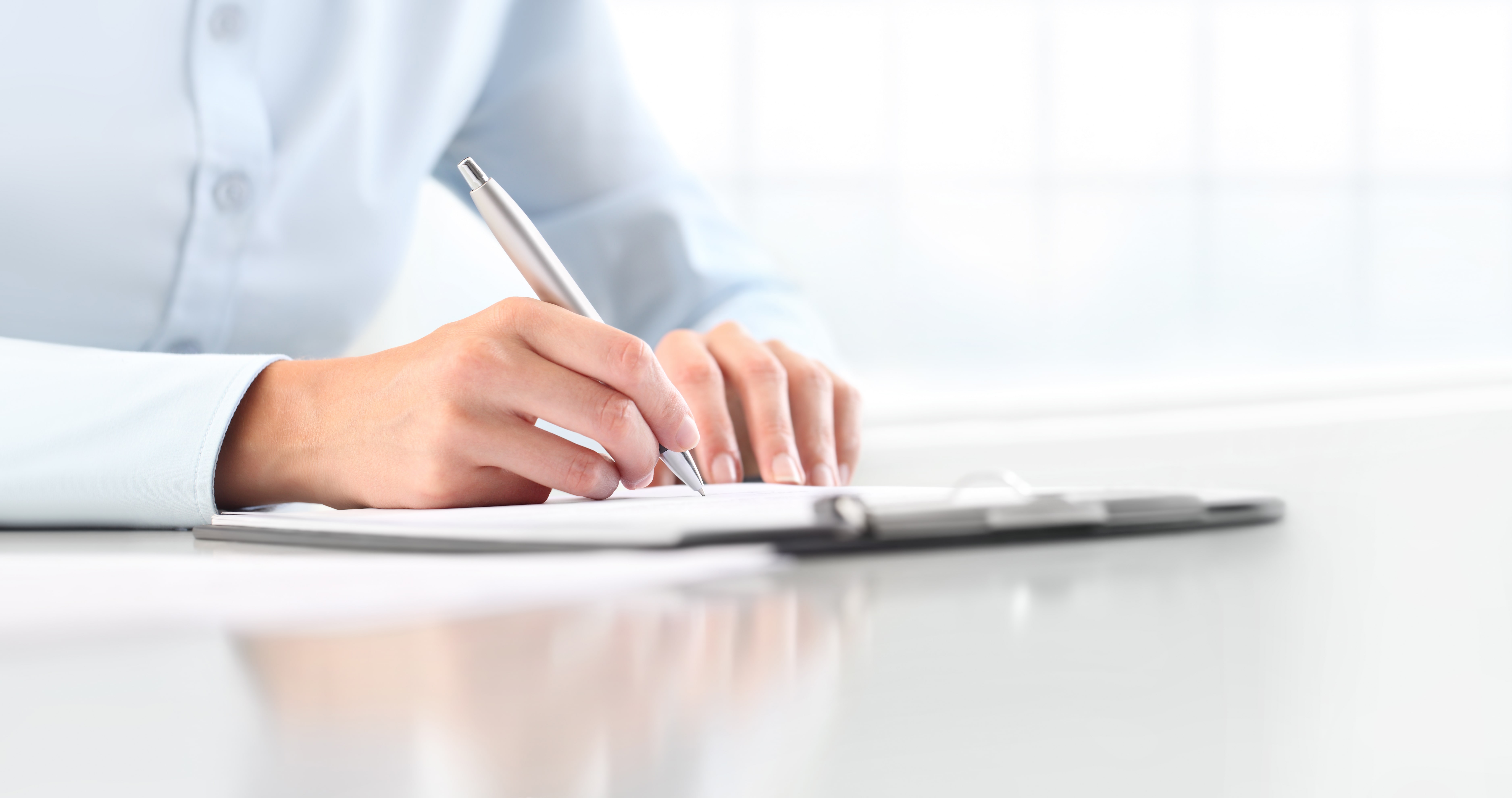 Woman's hands writing on sheet in a clipboard with a pen, isolated on desk