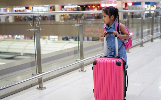 Cute Asian Child Girl With Backpack Holding Suitcase Waiting for Boarding In the Airport