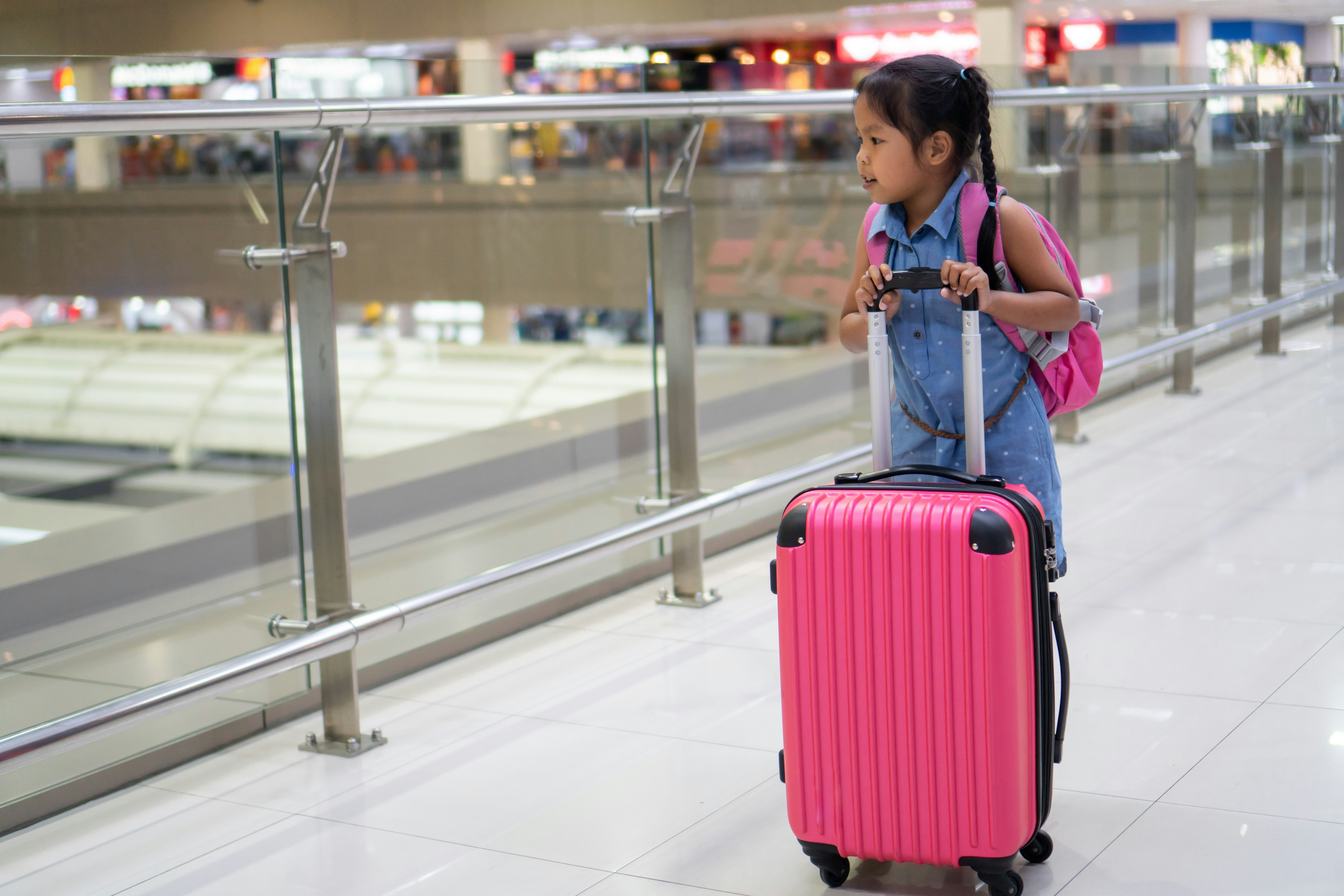 Cute Asian Child Girl With Backpack Holding Suitcase Waiting for Boarding In the Airport