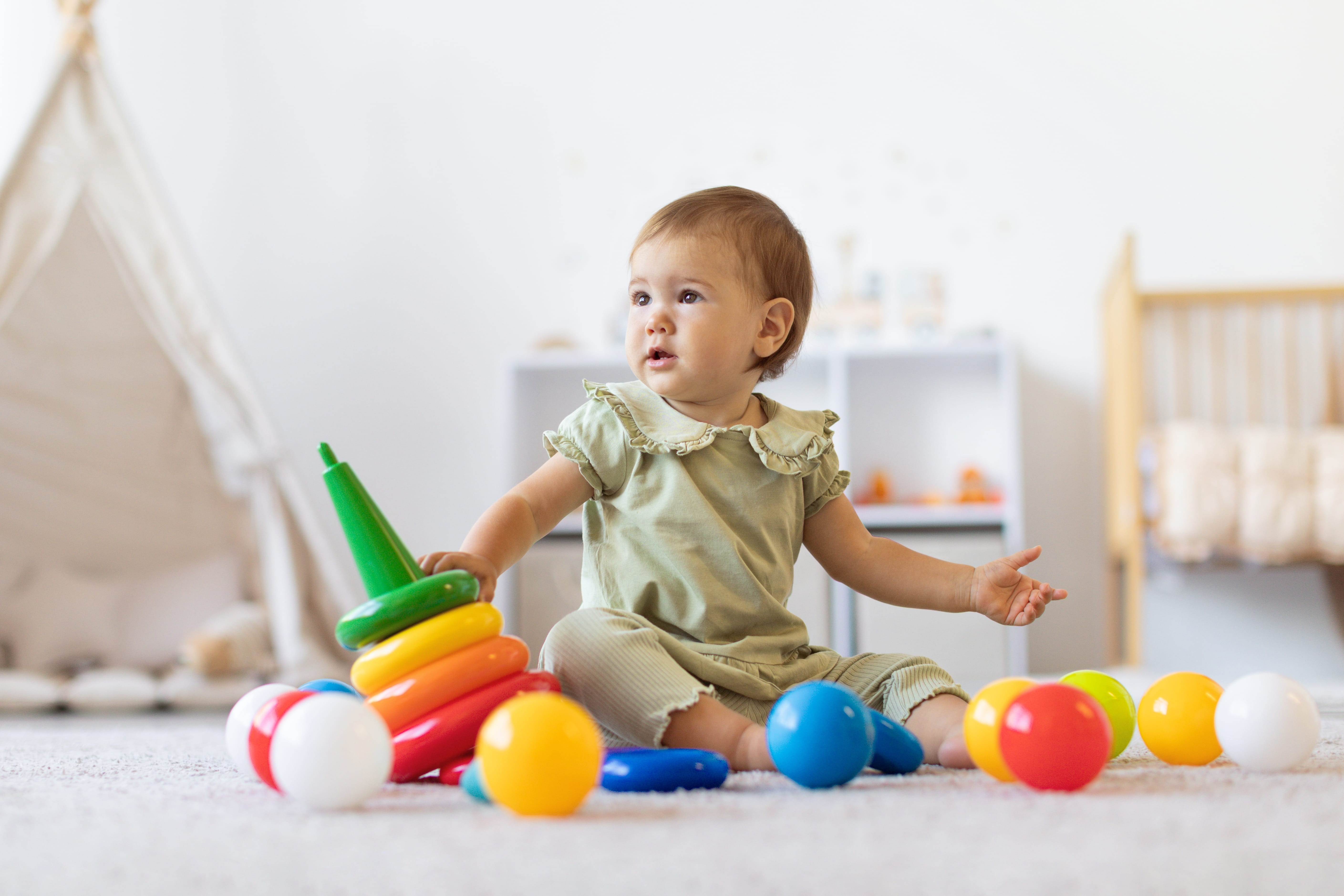 Cute Infant Baby Girl Sitting on Soft Carpet Surrounded by Colorful Toys