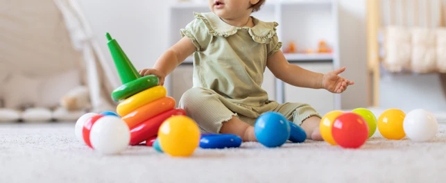 Cute Infant Baby Girl Sitting on Soft Carpet Surrounded by Colorful Toys