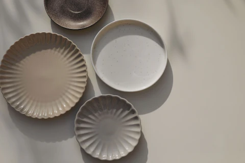 Different size and shapes of plates on beige table background in sunlight