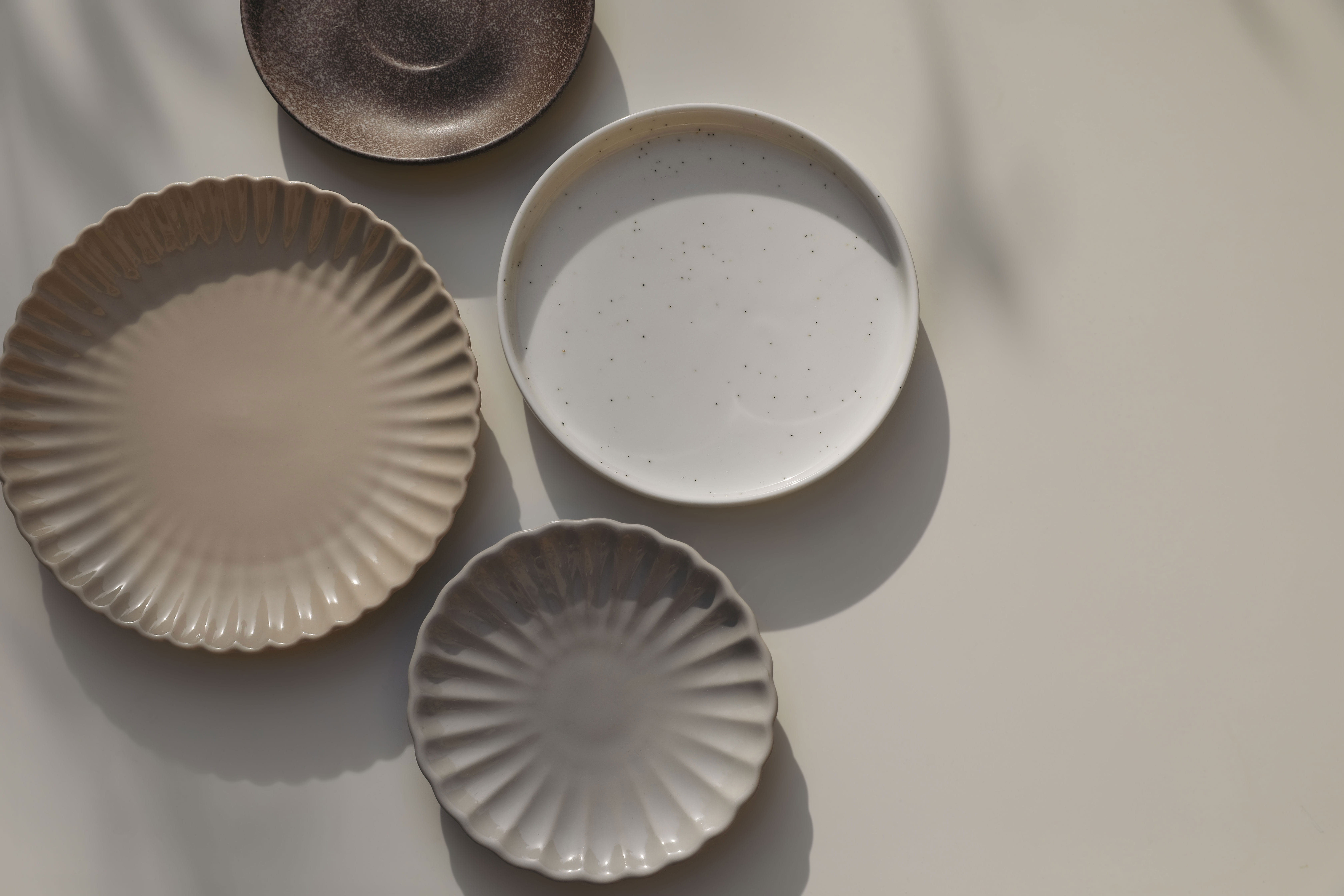Different size and shapes of plates on beige table background in sunlight