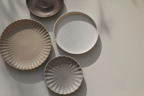 Different size and shapes of plates on beige table background in sunlight