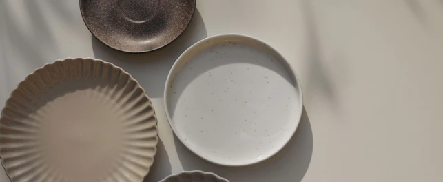 Different size and shapes of plates on beige table background in sunlight