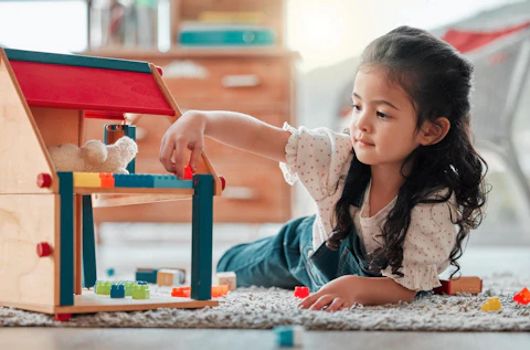 Girl, dollhouse and child play on floor, games and fantasy for brain development in home. Female person, toys and blocks on ground for entertainment, growth and toddler for education or learning