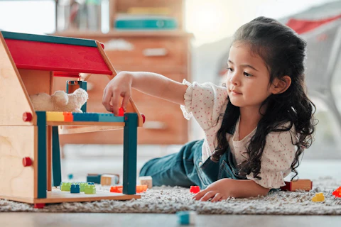 Girl, dollhouse and child play on floor, games and fantasy for brain development in home. Female person, toys and blocks on ground for entertainment, growth and toddler for education or learning