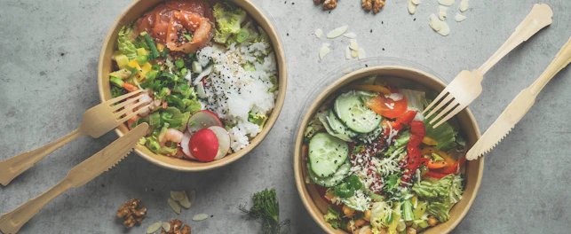 Japans poke bowl with seafood and salad and vegan bowl with vegetables and chickpeas in sustainable food container at grey background. Eco-friendly delivery food with plastic free cutlery. Top view.