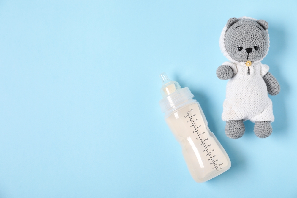 Feeding bottle with formula and toy bear on light blue background