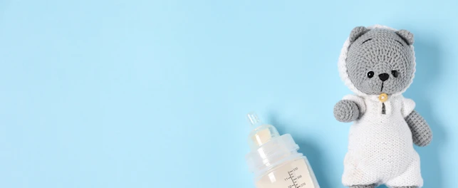 Feeding bottle with formula and toy bear on light blue background