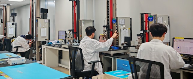 A laboratory setting with several people in lab coats seated at rubber material testing capability workstations.