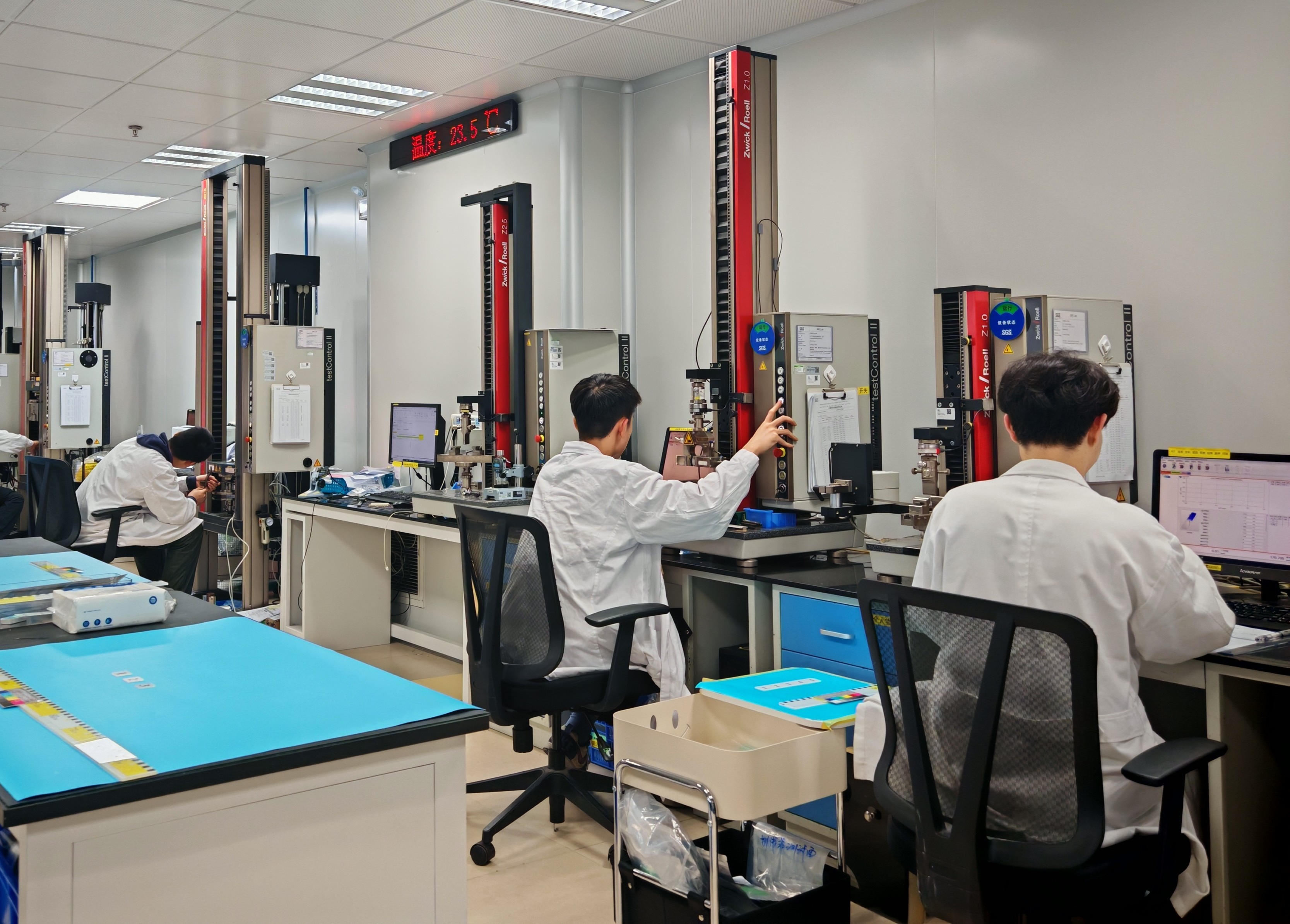 A laboratory setting with several people in lab coats seated at rubber material testing capability workstations.