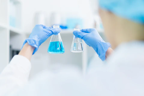 hand of scientist holding sample of chemical liquid in glassware comparing substance in laboratory