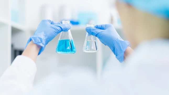 hand of scientist holding sample of chemical liquid in glassware comparing substance in laboratory