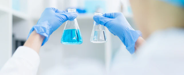 hand of scientist holding sample of chemical liquid in glassware comparing substance in laboratory