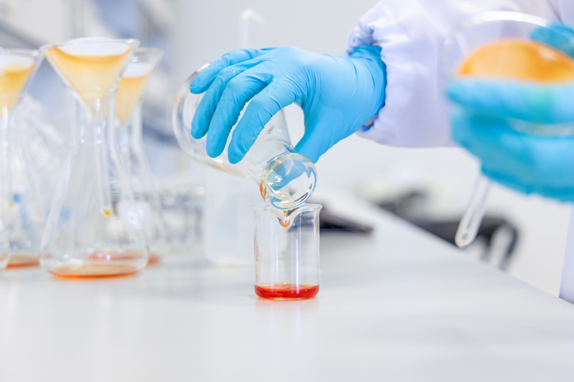 Hands pouring an orange chemical solution into a beaker