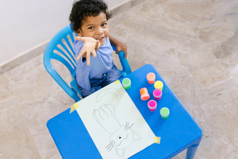 Happy Colombian Boy Having Fun Painting a Cat Drawing With Colorful Finger Paints at His Blue Table