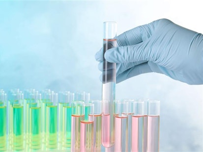 Analyse chimique en laboratoire avec tubes à essai colorés Main gantée tenant un tube à essai contenant un liquide coloré dans un laboratoire.