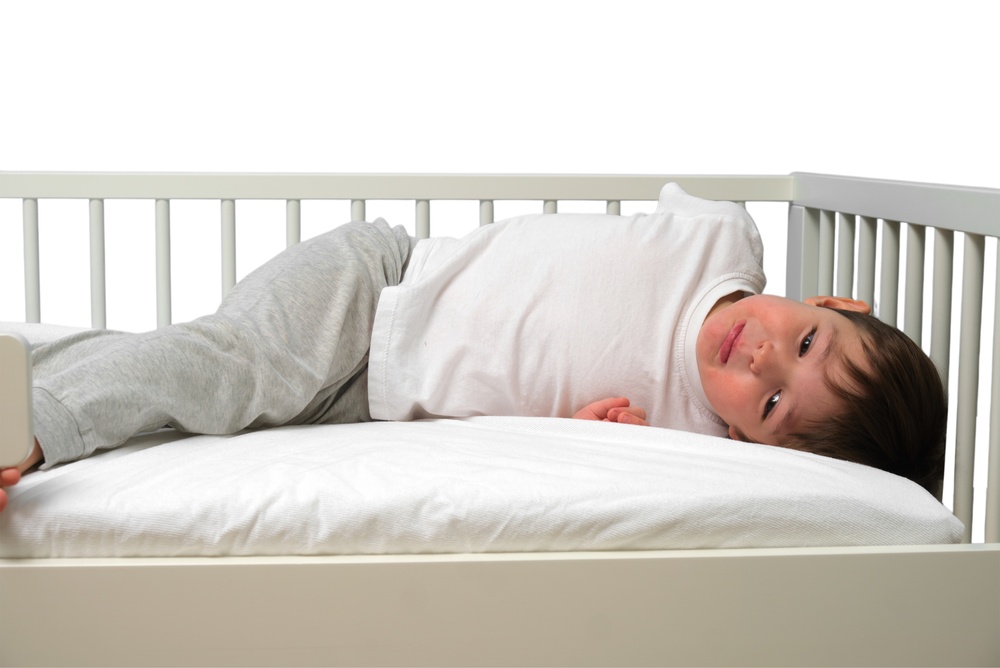 Little boy lying in white toddler bed