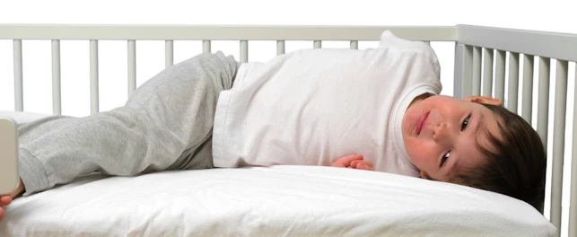 Little boy lying in white toddler bed