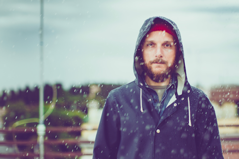 Man wearing a dark hooded jacket standing outdoors in the rain