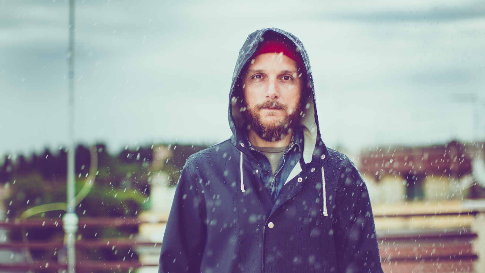 Man wearing a dark hooded jacket standing outdoors in the rain