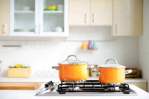 Deux casseroles orange sur une cuisinière à gaz dans une cuisine moderne blanche.