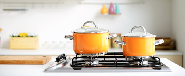 Deux casseroles orange sur une cuisinière à gaz dans une cuisine moderne blanche.