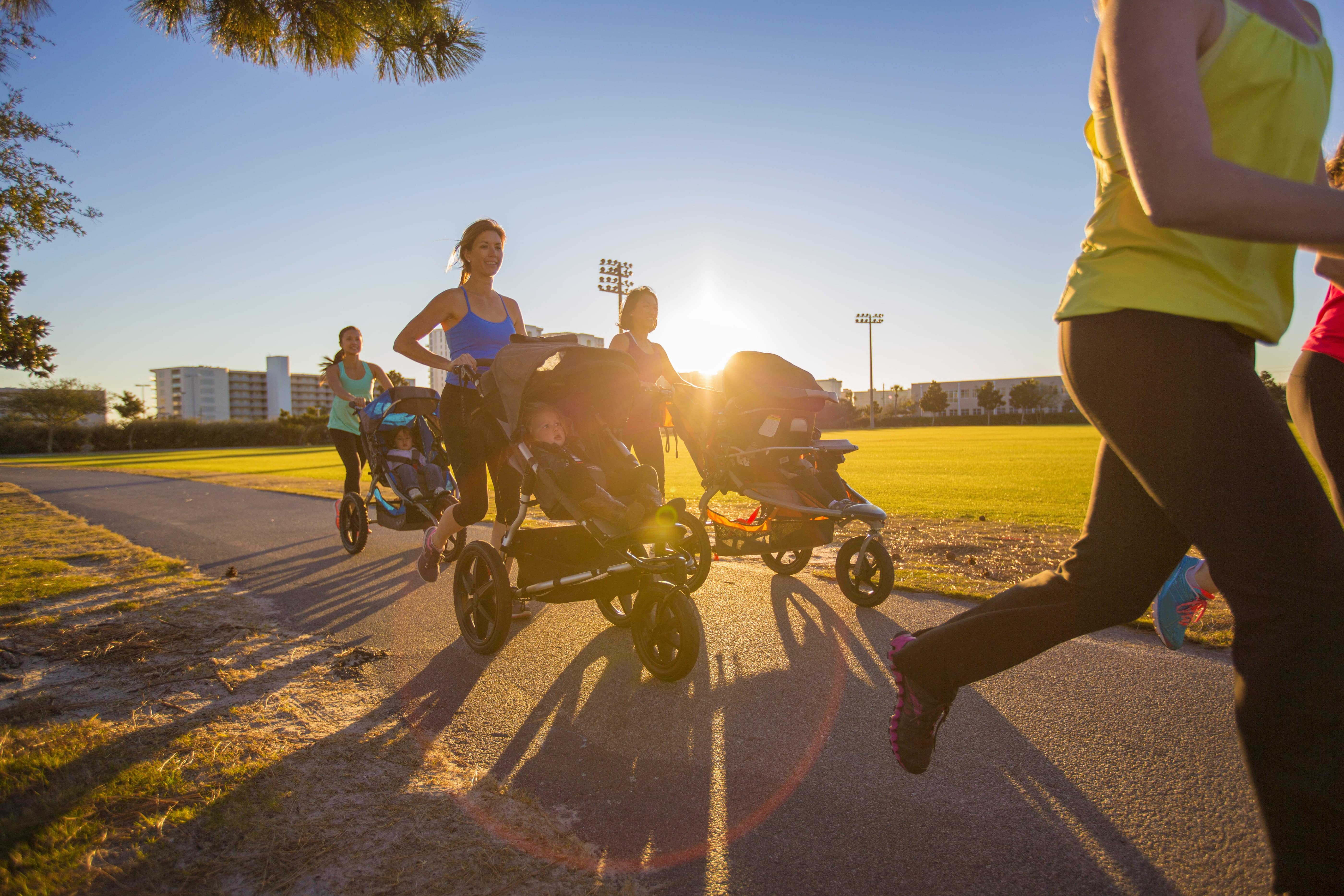 Femmes faisant du jogging avec des poussettes sportives sur une piste extérieure au coucher du soleil.