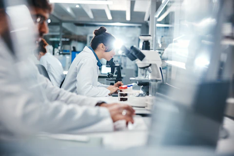 People in lab coats closely examining samples using microscopes and scientific equipment.