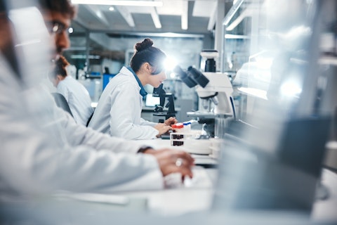 People in lab coats closely examining samples using microscopes and scientific equipment.
