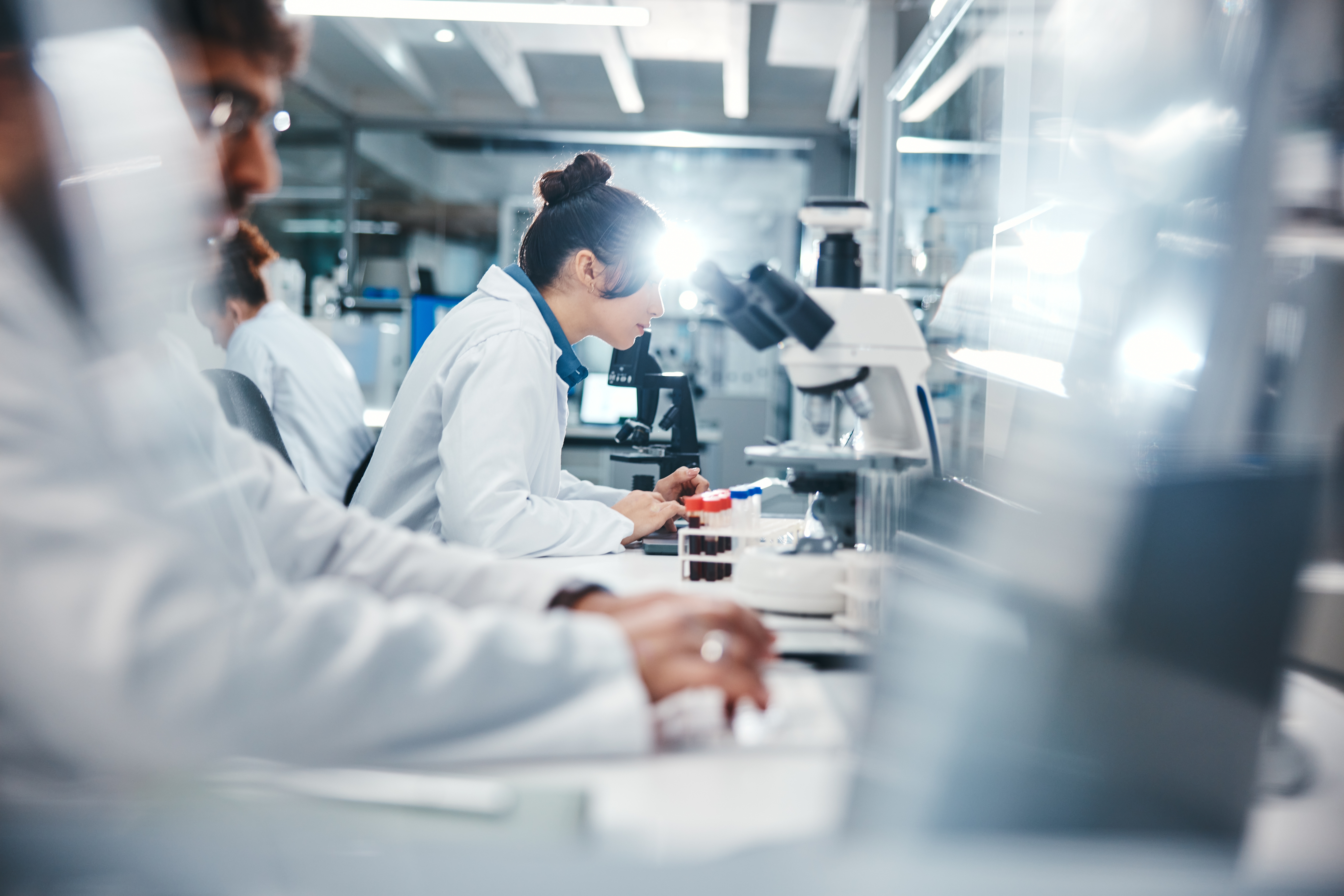 People in lab coats closely examining samples using microscopes and scientific equipment.