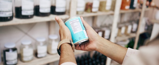 A person holding and reading the label on a packaged product inside a shop.