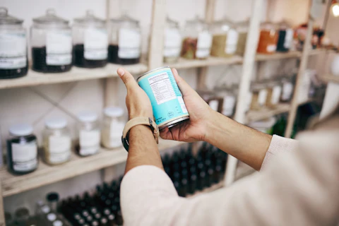 A person holding and reading the label on a packaged product inside a shop.