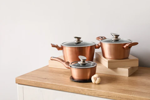 Set of Copper Cooking Pots with Garlic on Counter Near Light Wall