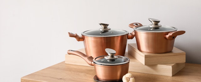 Set of Copper Cooking Pots with Garlic on Counter Near Light Wall