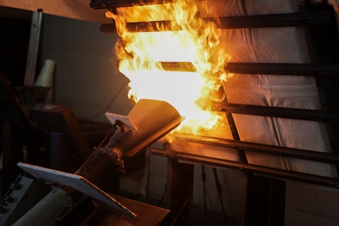 Intense industrial fire test, where a powerful flame is directed at a wall or panel structure to evaluate its fire resistance and performance under extreme heat.